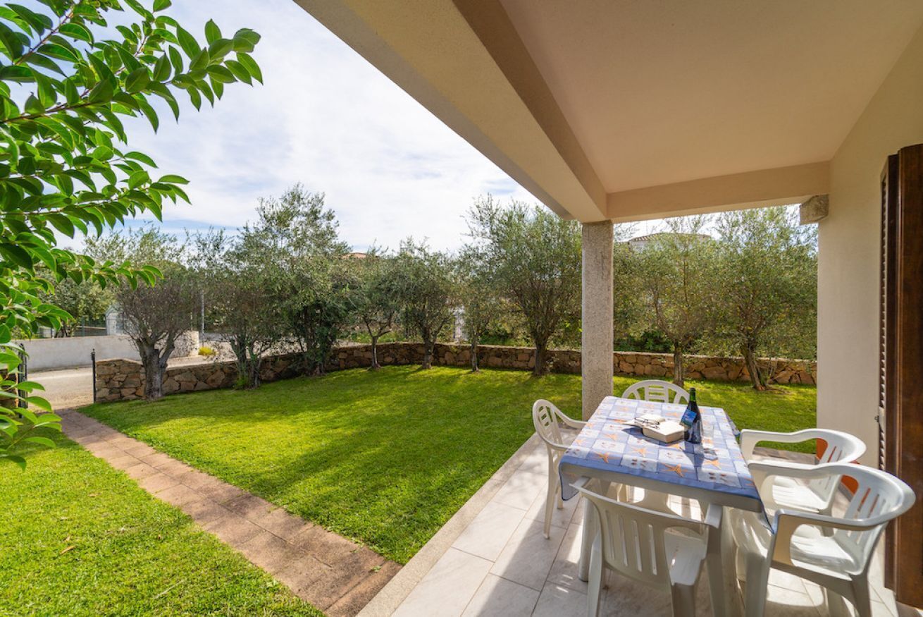 An outdoor patio with a table and chairs, surrounded by a well-maintained lawn and stone walls.