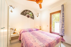 Une chambre à coucher comprenant un lit, une table de chevet, une commode et un ventilateur de plafond.