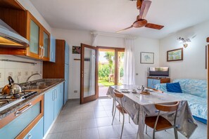 Une cuisine compacte équipée d’une cuisinière, d’un évier et de placards, un coin repas avec une table et des chaises, et un téléviseur dans un espace de vie agrémenté d’un canapé.