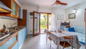 Eine kleine Küche mit Herd, Spüle und Schränken, ein Essbereich mit Tisch und Stühlen sowie ein Fernseher in einem Wohnbereich mit einer Couch.