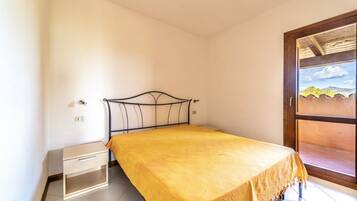 Un lit simple avec un cadre en métal et une couvre-lit jaune, dans une pièce aux murs blancs et au sol carrelé.
