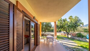 A covered outdoor patio with a table and chairs, a sliding door, and a view of a residential area with trees and a fence. - Gli Asfodeli Four-room apartment sleeps 6 (San Teodoro)