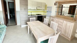 A compact kitchen with a dining table and chairs, a built-in oven, and a small refrigerator. - Gli Asfodeli Four-room apartment sleeps 6 (San Teodoro)