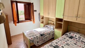 A bedroom with two beds, a window with curtains, and wooden cabinets. - Gli Asfodeli Four-room apartment sleeps 6 (San Teodoro)