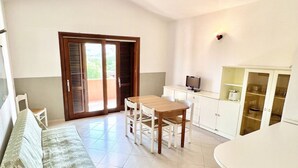 Un espacio habitable compacto con comedor, kitchenette y puerta corrediza de vidrio que da a un área exterior.