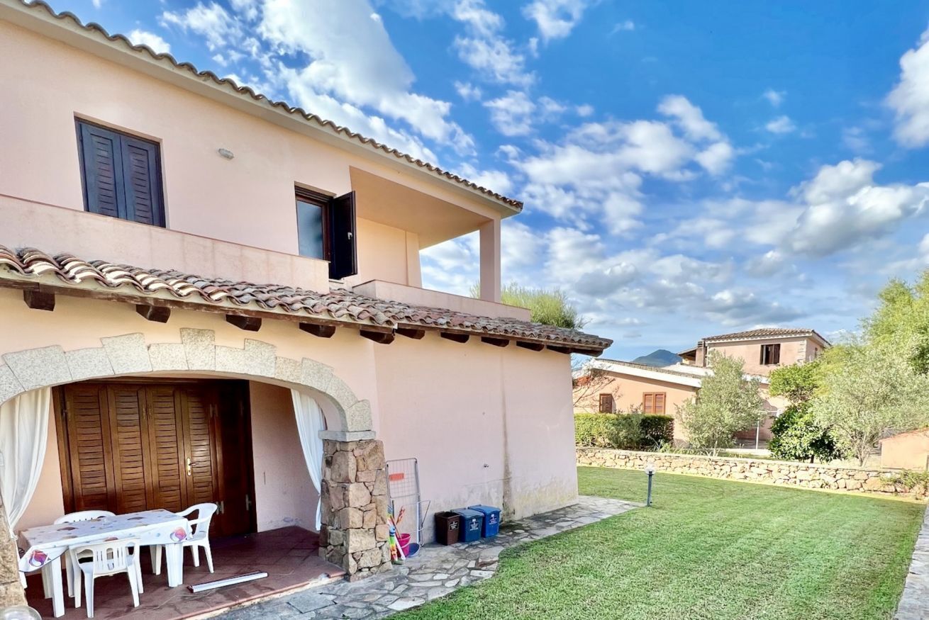 Un edificio su due piani con un ingresso ad arco in pietra, un patio con tavolo e sedie, e un prato curato.