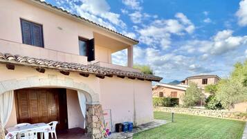 Un edificio su due piani con un ingresso ad arco in pietra, un patio con tavolo e sedie, e un prato curato.