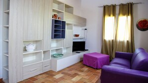 A compact living space with a built-in TV shelf, a purple sofa, and a tiled floor.