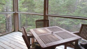 A wooden deck with a table and chairs, surrounded by a forest view.