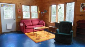 A wooden cabin interior with a red sofa, a green armchair, and a blue floor.