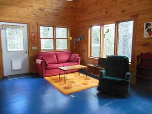 Interior acogedor de una cabaña con un sofá rojo, un sillón verde y un suelo azul.