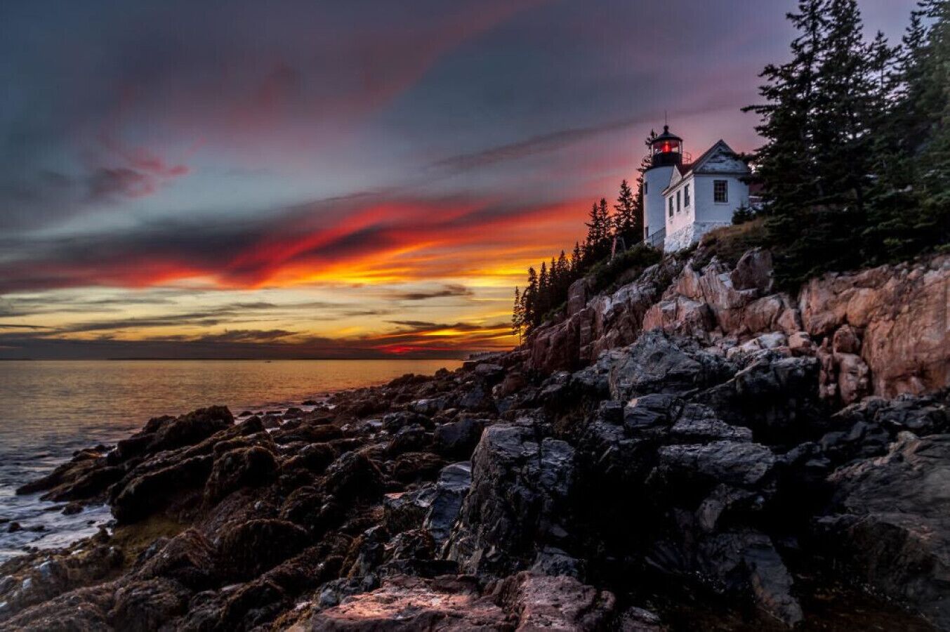 Un phare sur une côte rocheuse, avec un coucher de soleil en arrière-plan.
