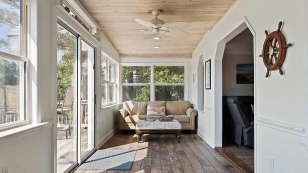 A sunlit room with a wooden ceiling, a large window, a beige sofa, and a coffee table. - Happy Place! Golf Cart Included! (Emerald Isle)