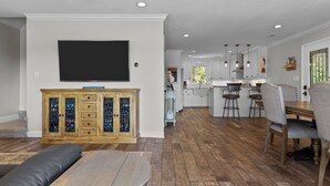 A modern kitchen with white cabinets, a large flat-screen TV, and a dining area with a wooden table and chairs. - Happy Place! Golf Cart Included! (Emerald Isle)