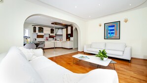 Una sala de estar moderna con un sofá blanco, una mesa de centro y un comedor con una cocina visible a través de un arco.