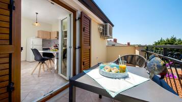 Un balcón con una mesa dispuesta para el desayuno, una cocina visible a través de una puerta abierta, y una escultura decorativa con forma de pez.