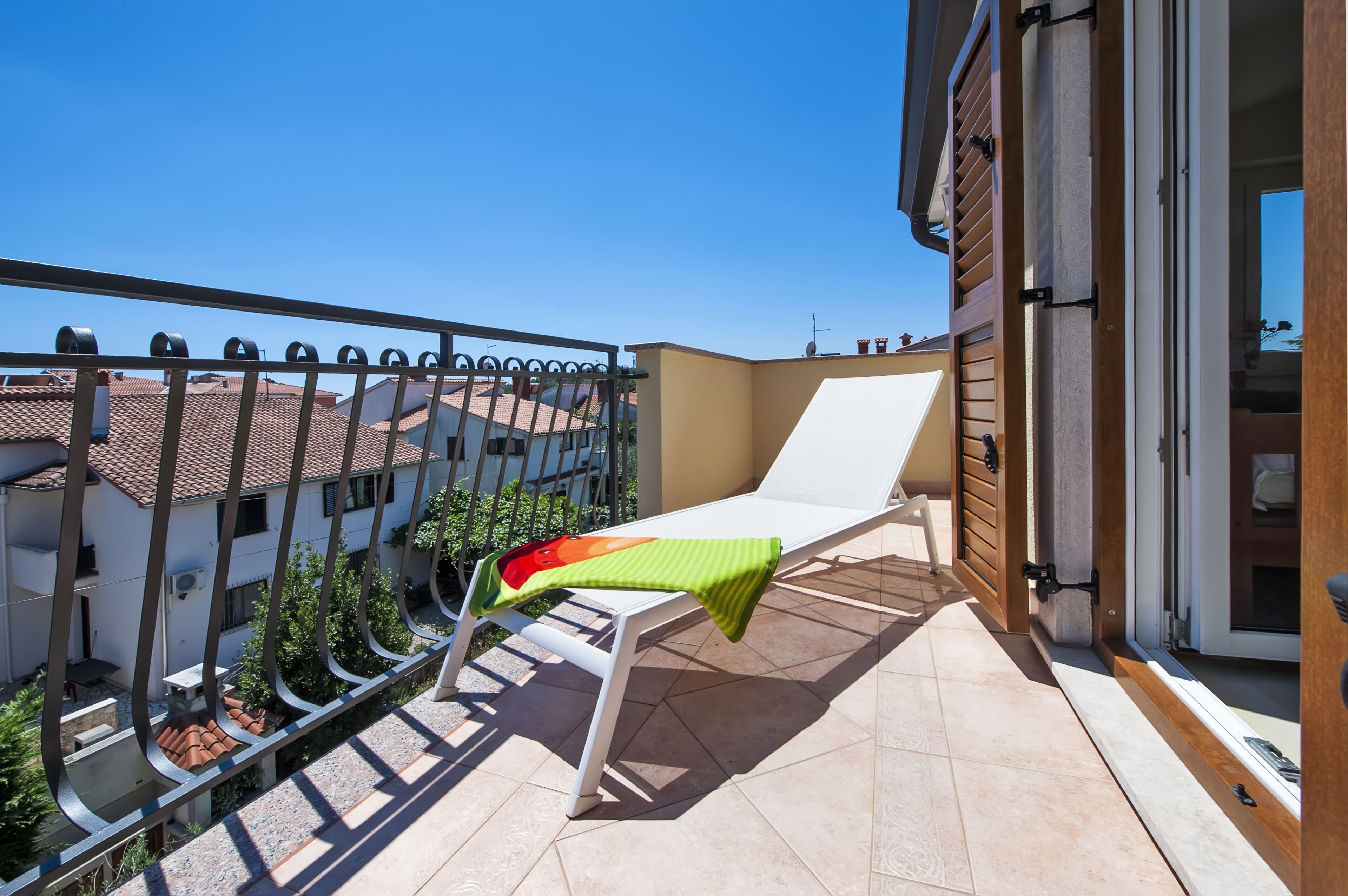 A balcony with a white lounge chair, a metal railing, and a view of neighboring buildings.