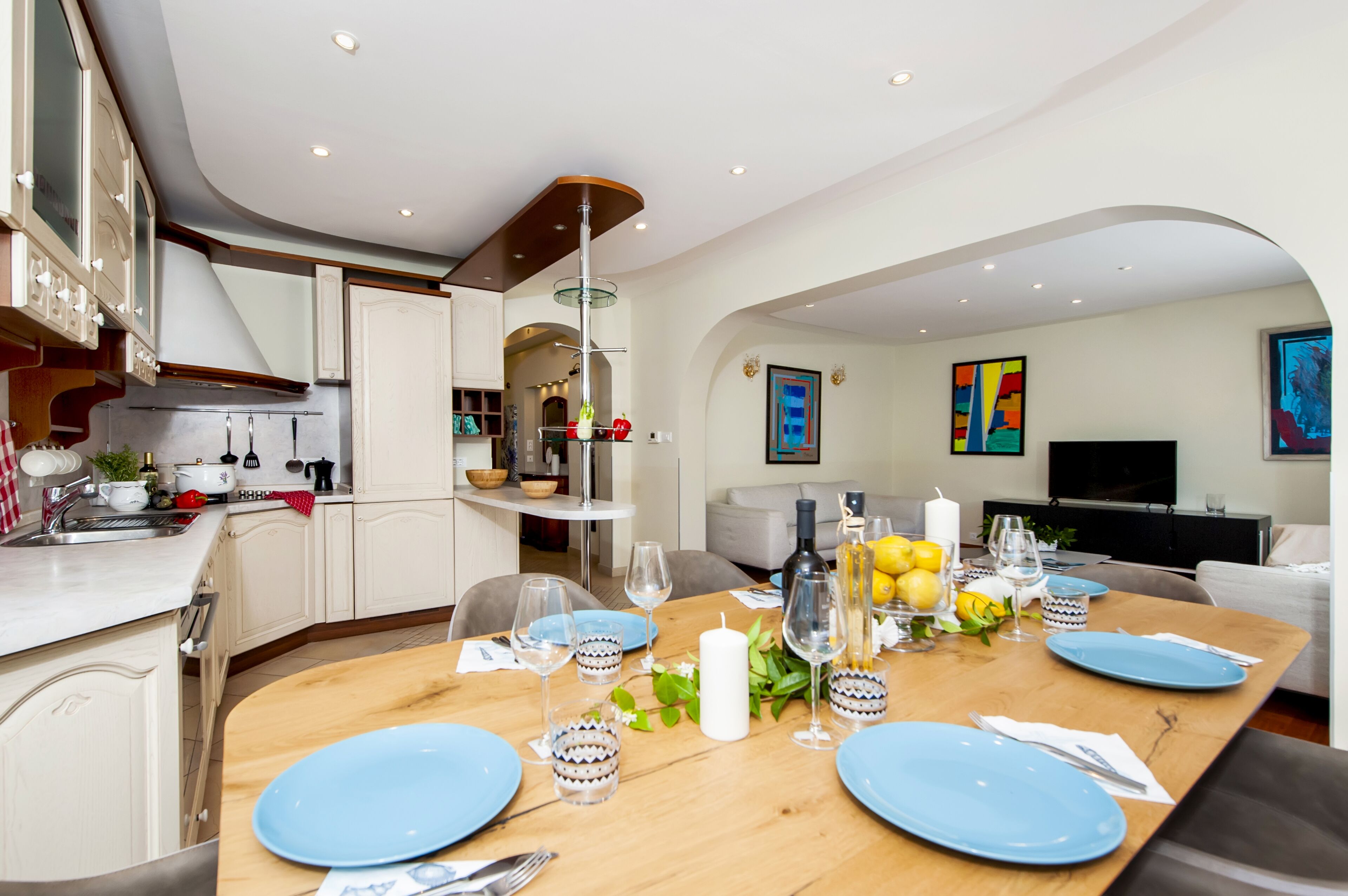 A modern kitchen with white cabinets, a dining area with blue plates, and a living room with a TV.