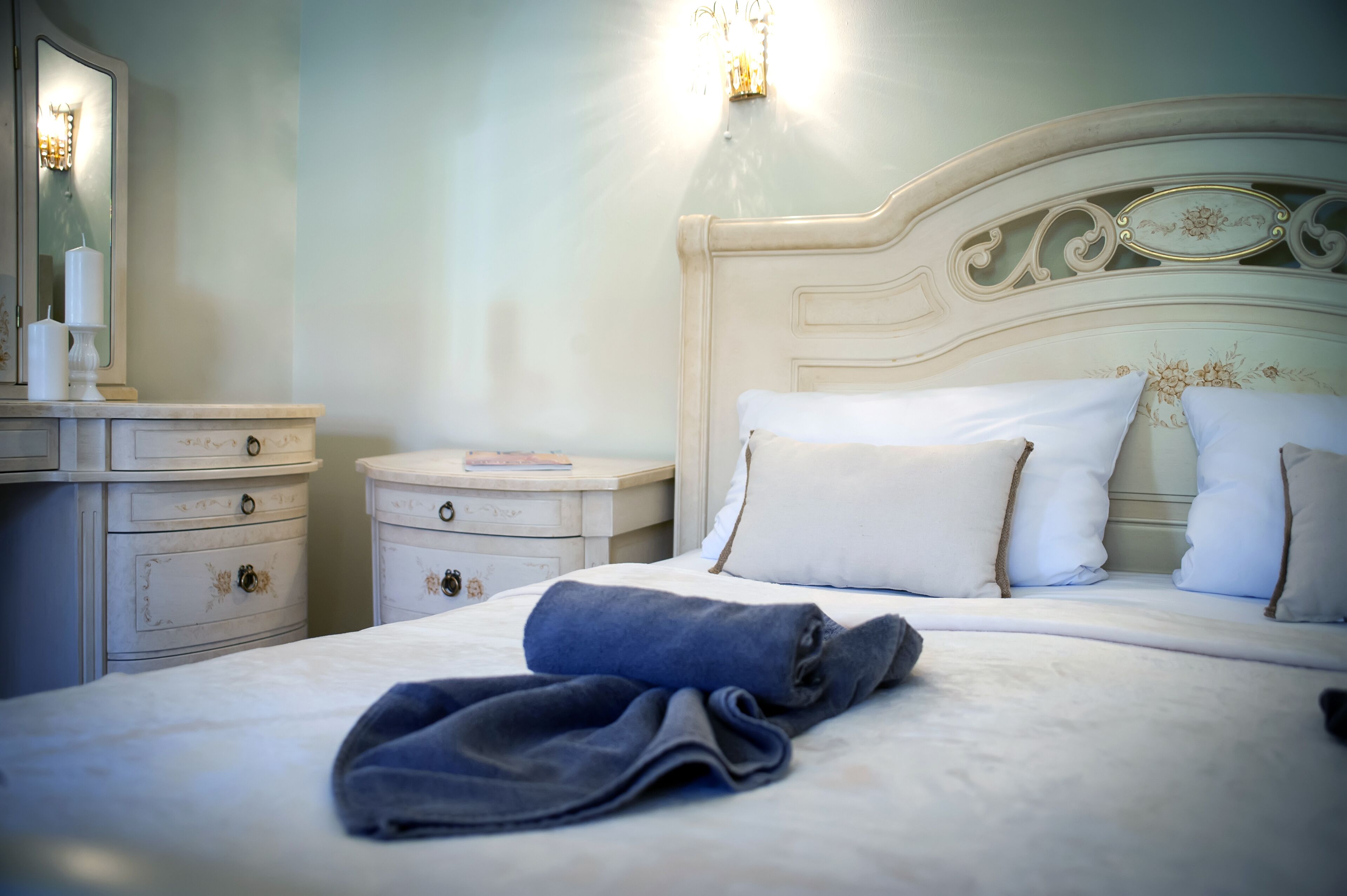 A neatly made bed with a folded towel, a nightstand with a lamp, and a dresser with drawers.