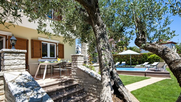 Una escalera de piedra conduce a un área de piscina con mobiliario exterior y una mesa de comedor.