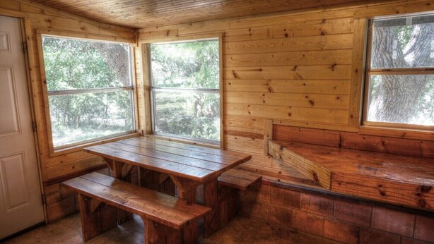 A wooden cabin with a large windowed porch, a wooden bench, and a stone fireplace. - Zubers - CA -C Cabin C (Concan)