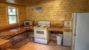 A compact kitchen with wooden walls, a stove, a microwave, and a refrigerator. - Zubers - CA -C Cabin C (Concan)