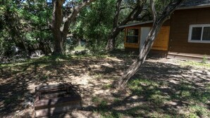 A cabin with a wooden exterior, surrounded by trees and a small fire pit area. - Zubers - CA -C Cabin C (Concan)