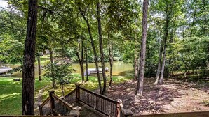 A wooden deck leading to a forested area with a lake. - Breathtaking porch just steps from the water. (Eatontonton)