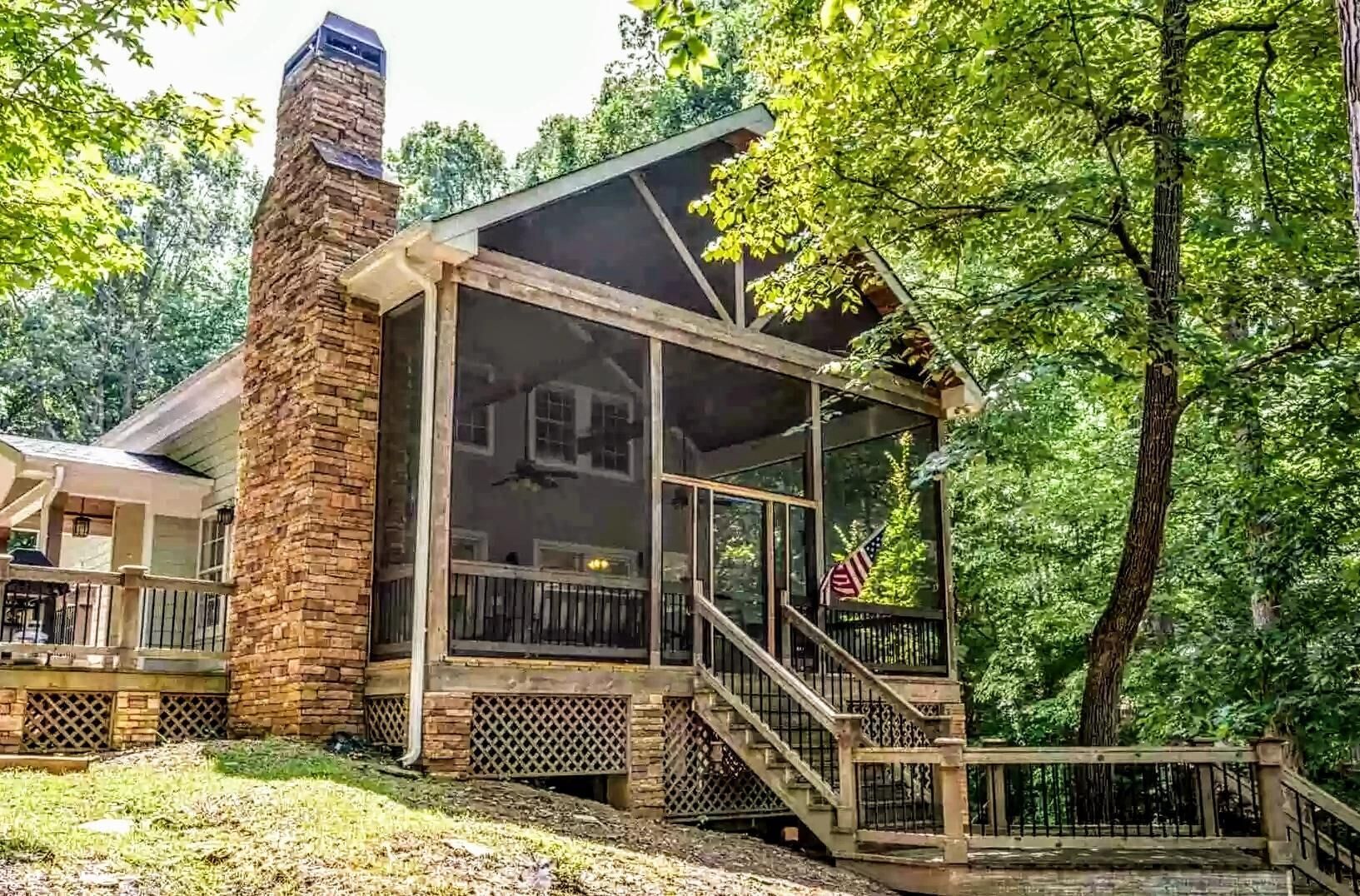 A cabin with a stone chimney, a covered porch, and a view of the surrounding forest.