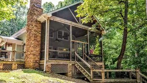 A cabin with a stone chimney, a covered porch, and a view of the surrounding forest. - Breathtaking porch just steps from the water. (Eatontonton)