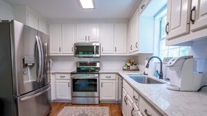 A modern kitchen with white cabinets, stainless steel appliances, a built-in oven, a microwave, and a sink. - Breathtaking porch just steps from the water. (Eatontonton)