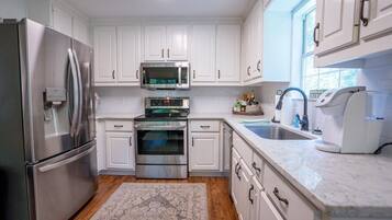 A modern kitchen with white cabinets, stainless steel appliances, a built-in oven, a microwave, and a sink.