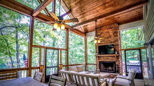 A cozy cabin with a stone fireplace, wooden furniture, and large windows offering a view of the forest. - Breathtaking porch just steps from the water. (Eatontonton)