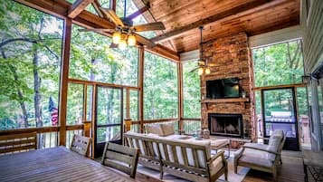 A cozy cabin with a stone fireplace, wooden furniture, and large windows offering a view of the forest.