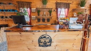 A wooden reception desk with a computer, a cash register, and a display of snacks. - Waterfront Log Cabin Hideaway Sauna Trails (Bethlehem)