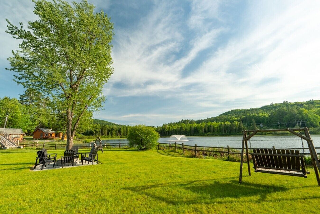 Un espace extérieur verdoyant avec une balançoire en bois, une clôture en bois et une étendue d’eau en arrière-plan.