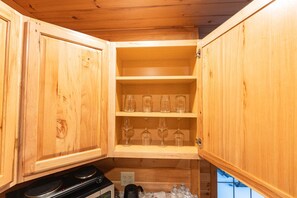 A wooden kitchen with open cabinets, a stove, and glassware on shelves.