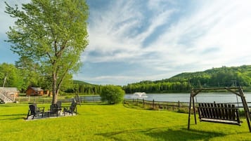 A grassy outdoor area with a wooden swing, a wooden fence, and a body of water in the background.
