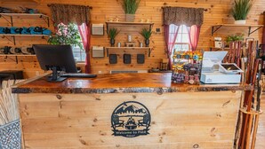 A wooden reception desk with a computer, a cash register, and a display of snacks. - Lakefront Log Cabin Hideaway for Two (Bethlehem)