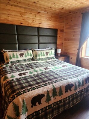 A bed with a quilt featuring bear and tree patterns, a dark headboard, and a wooden cabin interior. - Pet-Friendly Log Cabin | White Mountains (Bethlehem)