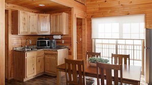 Una cabaña de madera con cocina que incluye microondas, pileta y alacenas, además de un comedor con mesa y sillas.