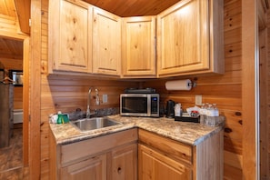 A wooden cabin interior with a kitchen featuring a granite countertop, stainless steel sink, microwave, and wooden cabinets. - Spacious Couples Log Cabin White Mountains (Bethlehem)
