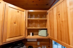 A wooden kitchen with shelves holding wine glasses and a toaster.