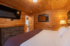 A wooden-paneled room with a bed, a TV, a dresser, and a door leading outside.