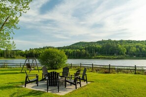 A lakeside outdoor seating area with Adirondack chairs and a swing set.