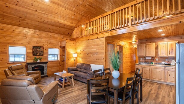 Interior de una cabaña de madera con sala de estar, comedor, cocina y una escalera.