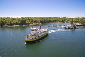 A riverboat with a white and yellow hull, docked at a pier with other boats and a forested shoreline in the background. - Historic Officer's Quarters House on Great Diamond Island Near Beaches (Portland)