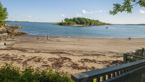 Ein Strand mit einer Holzpromenade, die zum Wasser führt, eine kleine Insel in der Ferne und ein klarer Himmel.