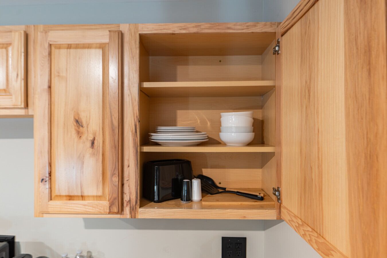 Un meuble de cuisine en bois, doté d’étagères, contenant des assiettes, des bols, une machine à café et une bouilloire.