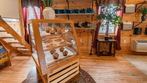 A bakery display case with pastries, a wooden staircase, and a rustic interior with wooden walls and a plant.